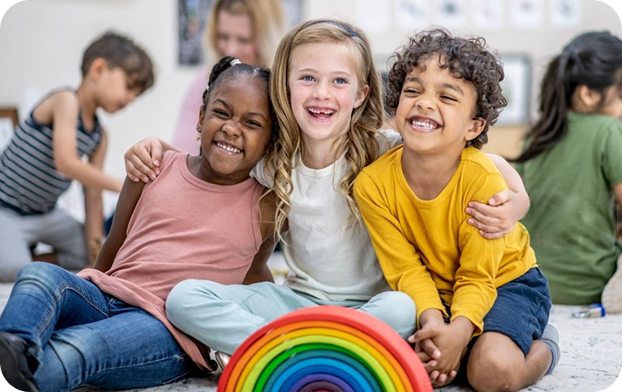 Three children smiling with a colorful rainbow toy.