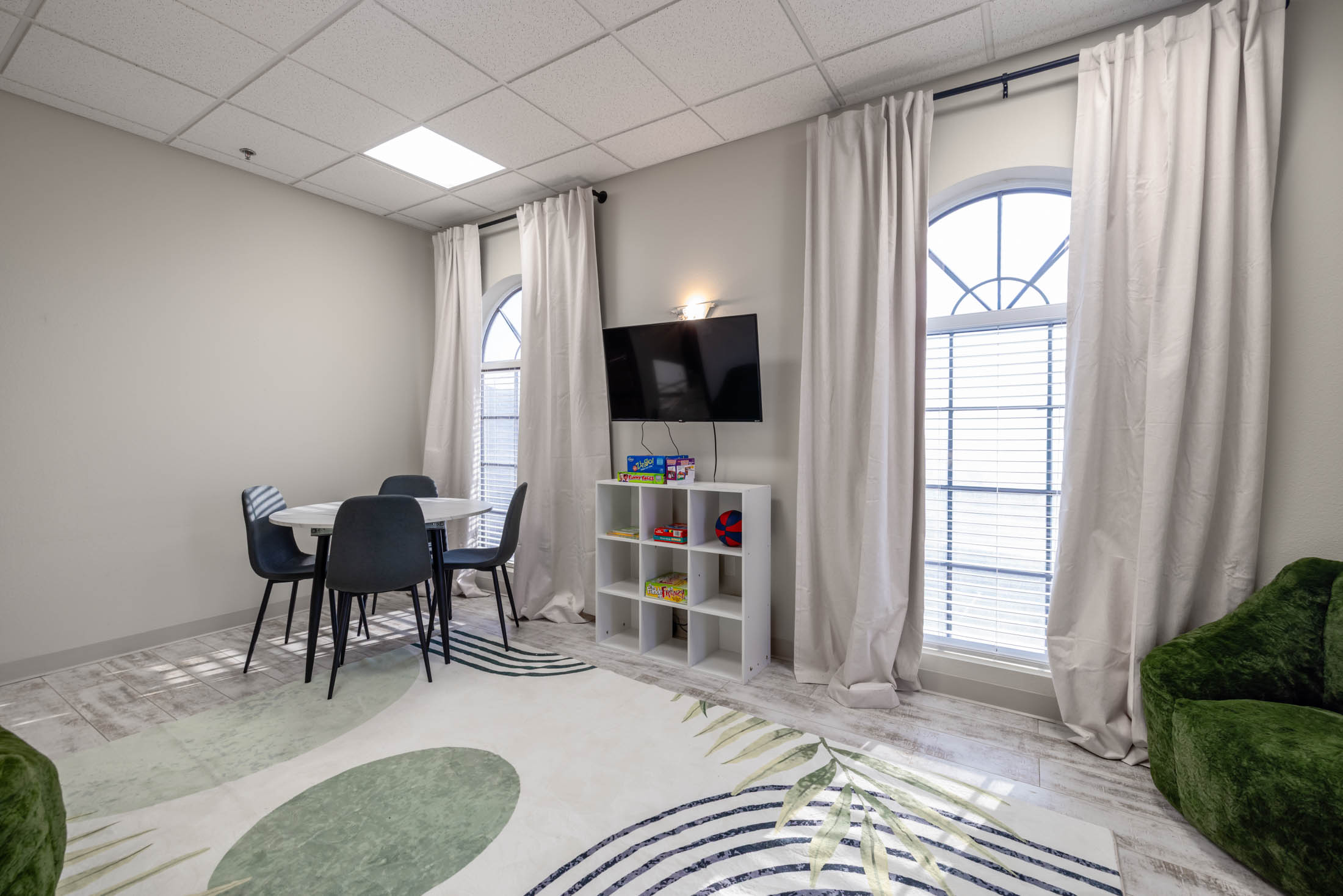 Bright, modern room with large windows, a round table, and a TV on the wall.