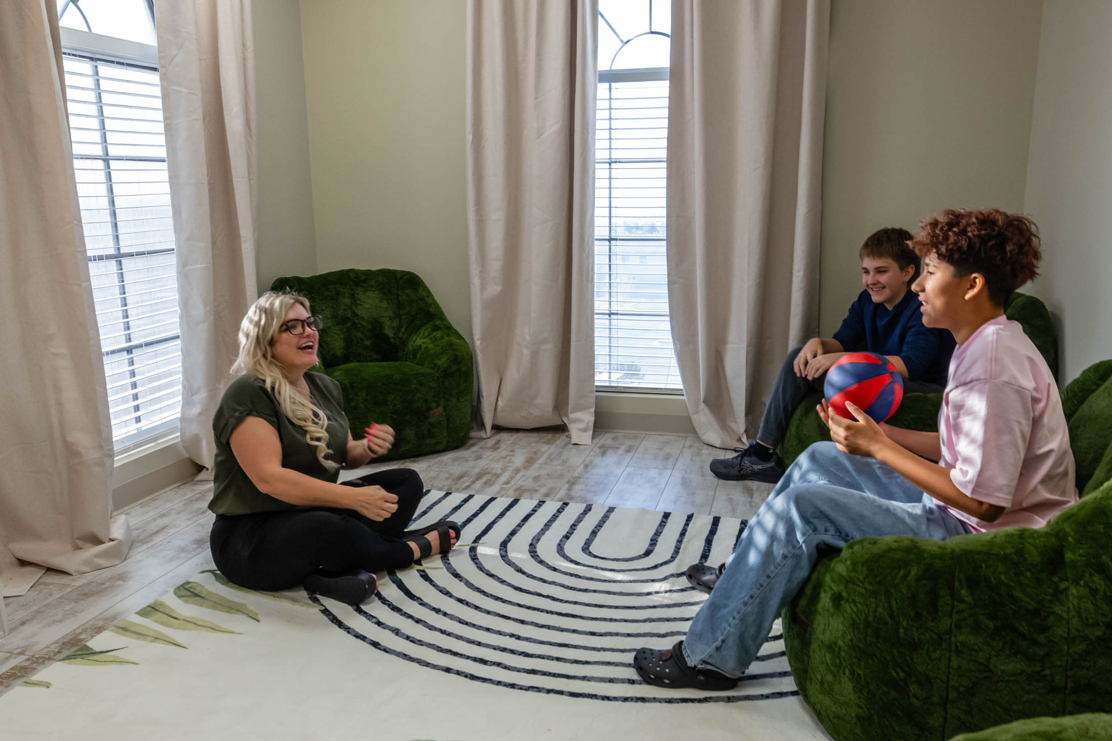 Three people sitting in a cozy room with green furniture and a circular rug.
